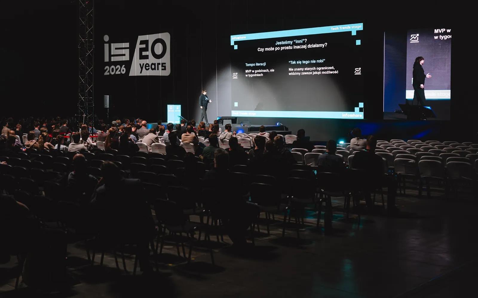 Kuba na scenie Tech Trends Infoshare 2026, przed nim widownia, obok slajd „Jesteśmy »inni«?”